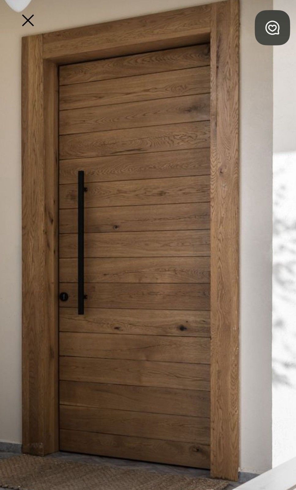 Una moderna puerta de madera compuesta por tablones horizontales con una manilla larga y vertical de color negro mate, enmarcada por madera clara a juego.