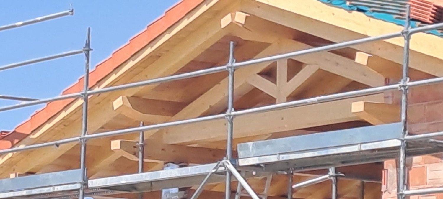 Primer plano de una cercha de madera en construcción, enmarcada por andamios metálicos contra un cielo azul despejado.