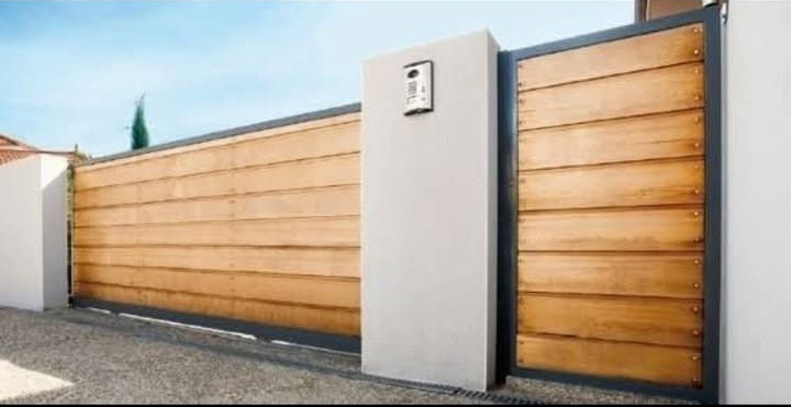 Una puerta corredera de madera con tablones horizontales y una puerta peatonal a juego junto a una pared blanca con un interfono.