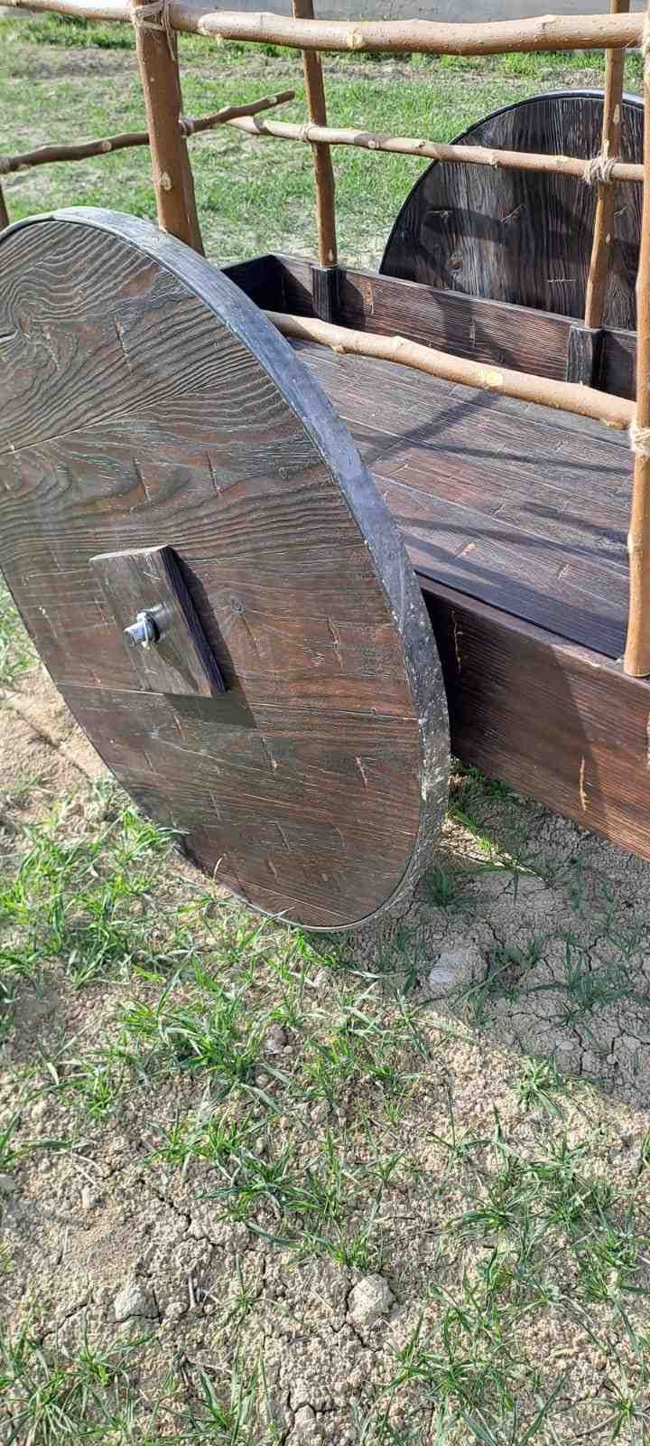 Un carro de madera con grandes ruedas circulares de madera y una barandilla rústica, apoyado sobre la hierba.
