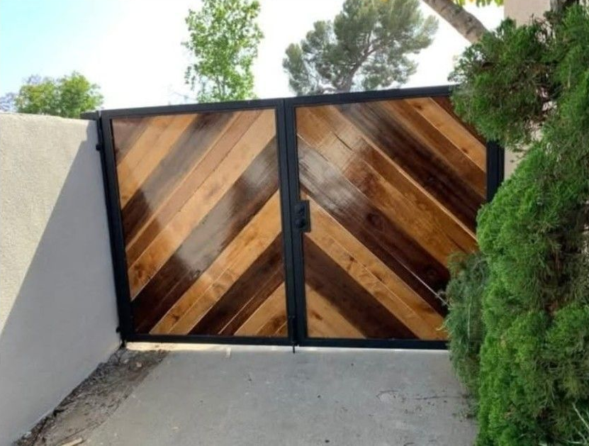 Puerta doble con tablones de madera oscura y clara dispuestos en forma de espiga diagonal dentro de un marco de metal negro.