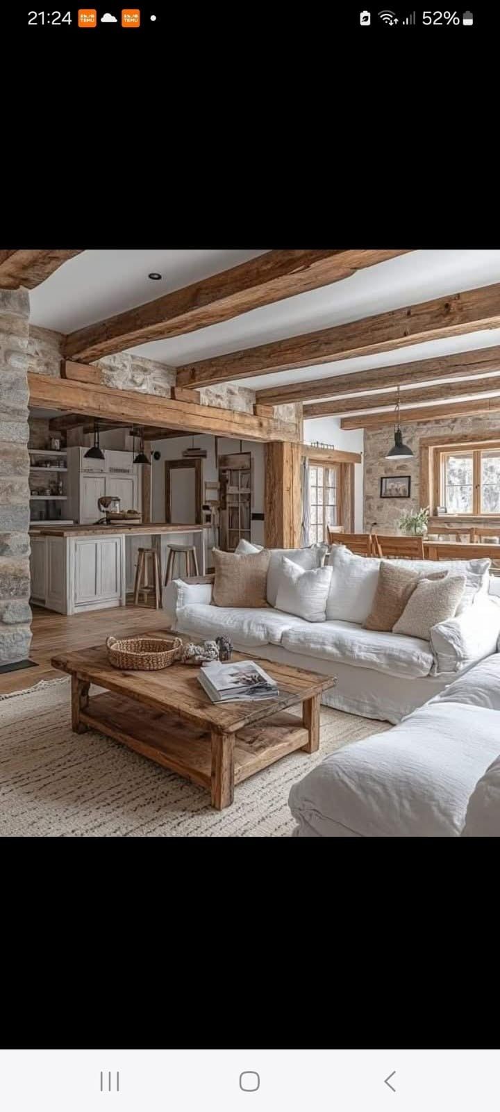 Un salón rústico con vigas de madera a la vista en el techo, paredes de piedra, un sofá blanco y una mesa de centro de madera.