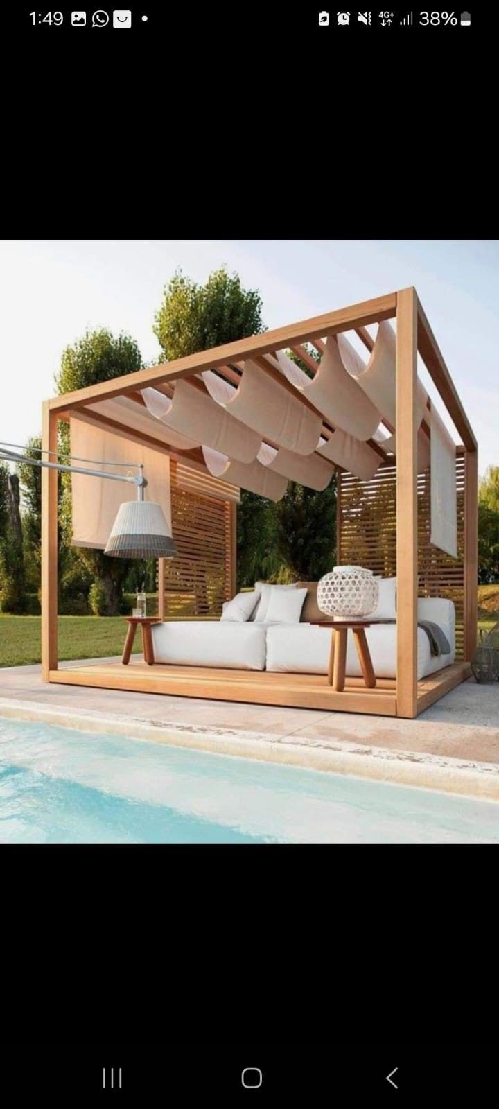 Una cabaña de madera con toldo de tela beige, un sofá blanco de exterior y pequeñas mesas de madera junto a la piscina.