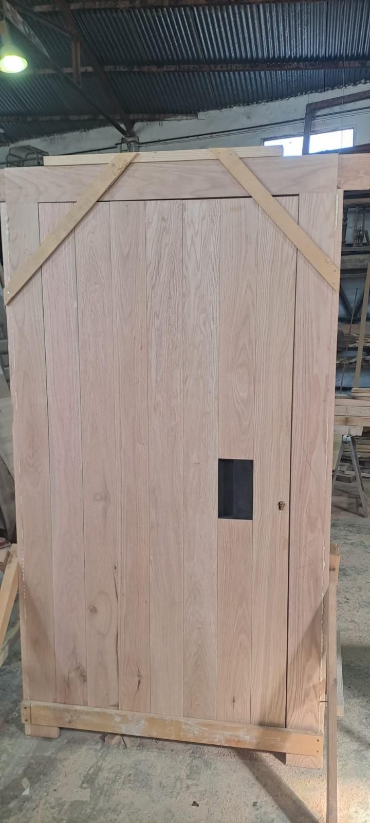 Una puerta de madera con un hueco rectangular para el tirador, reforzada con tirantes diagonales de madera, situada en un taller.