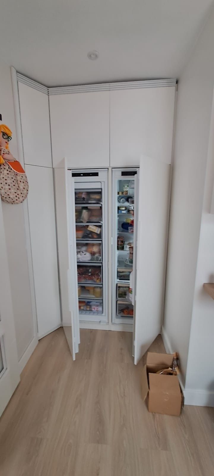 Una zona de cocina estrecha con dos frigoríficos/congeladores blancos empotrados, colocados uno al lado del otro, con las puertas abiertas.