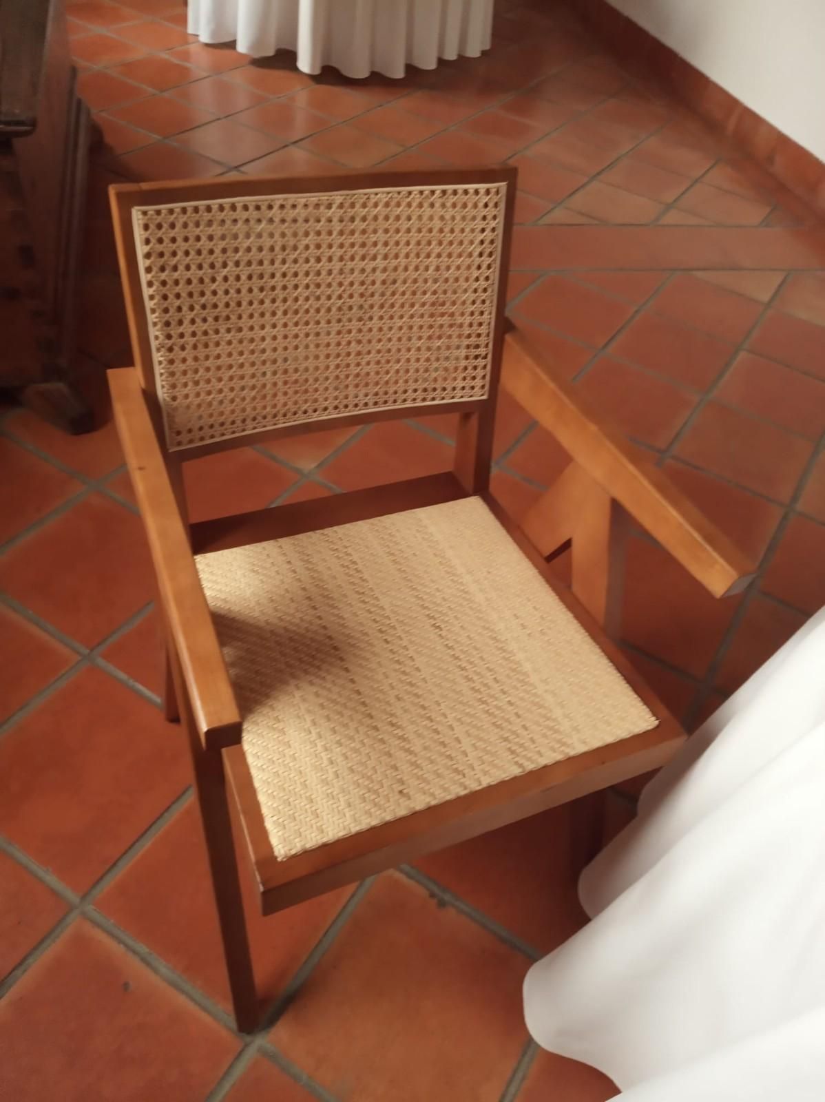 Un sillón de madera con respaldo y asiento de ratán tejido, situado sobre un suelo de baldosas de terracota.