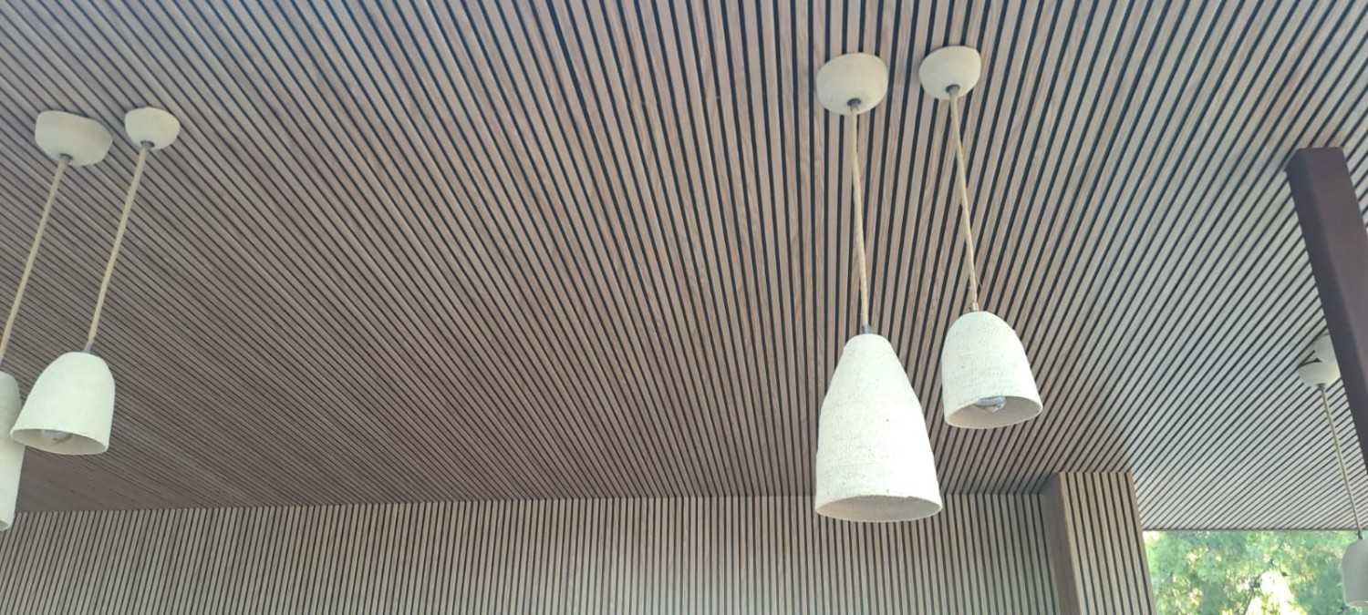 En un espacio moderno, cuatro lámparas colgantes blancas cuelgan de un techo de listones de madera.