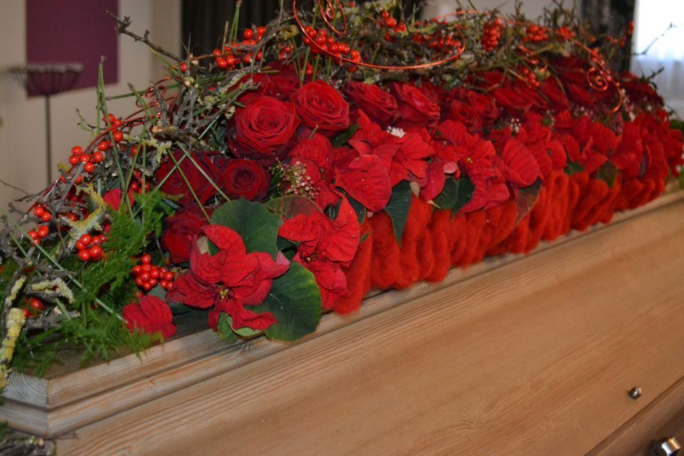 Sargdeckel verkleidet mit einem Blumengesteck aus roten Rosen, roten Blumen und Moos .