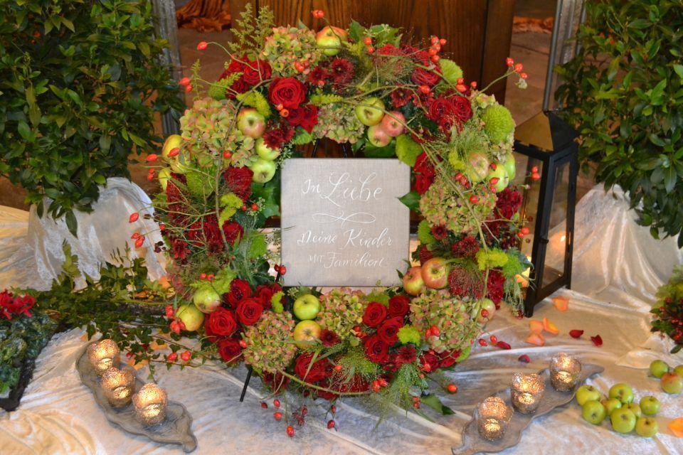 Runder Blumenkranz aus roten und grünen Blumen mit einer beschrifteten Tafel in der Mitte.