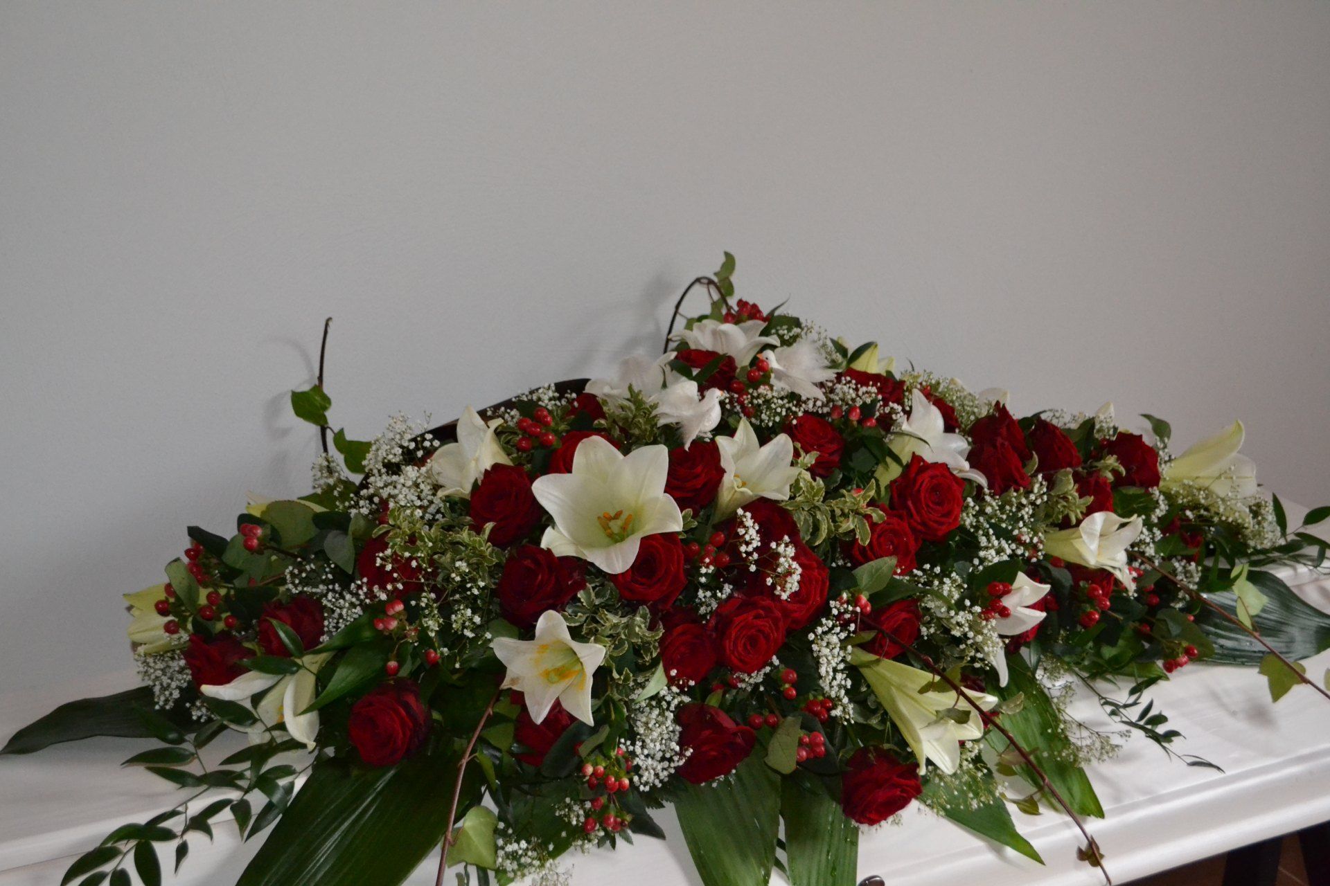 Blumengesteck mit weißen Lilien und roten Rosen auf einem Sarg.