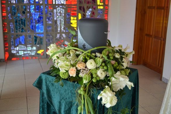 Ausgestelltes Blumengesteck um eine Urne auf einem Sockel