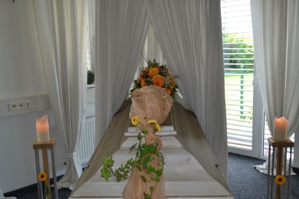 Blumenstrauß auf einem Sarg mit Kerzen und Schleier.