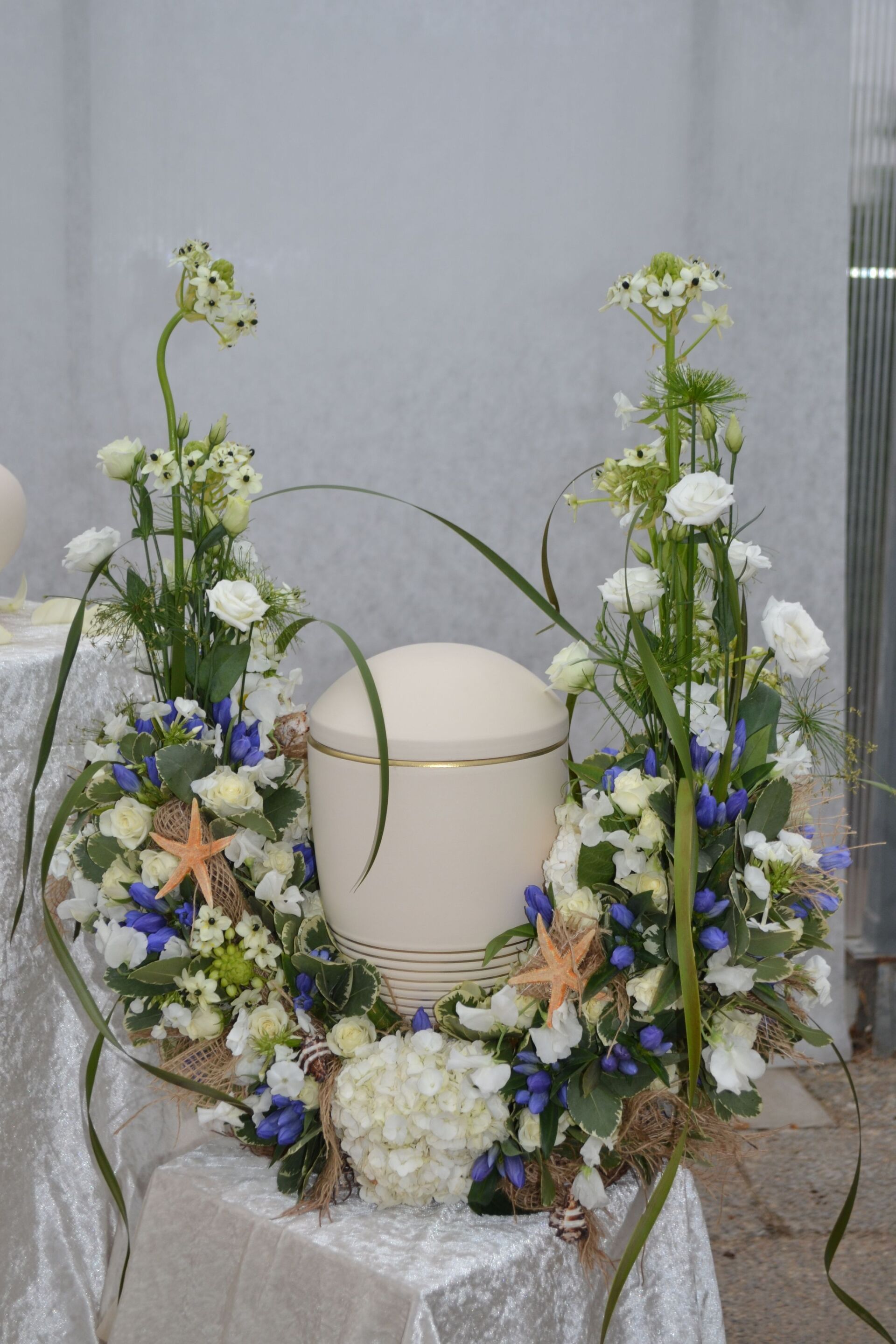 Hohe Blumengestecke um eine weiß-goldene Urne.