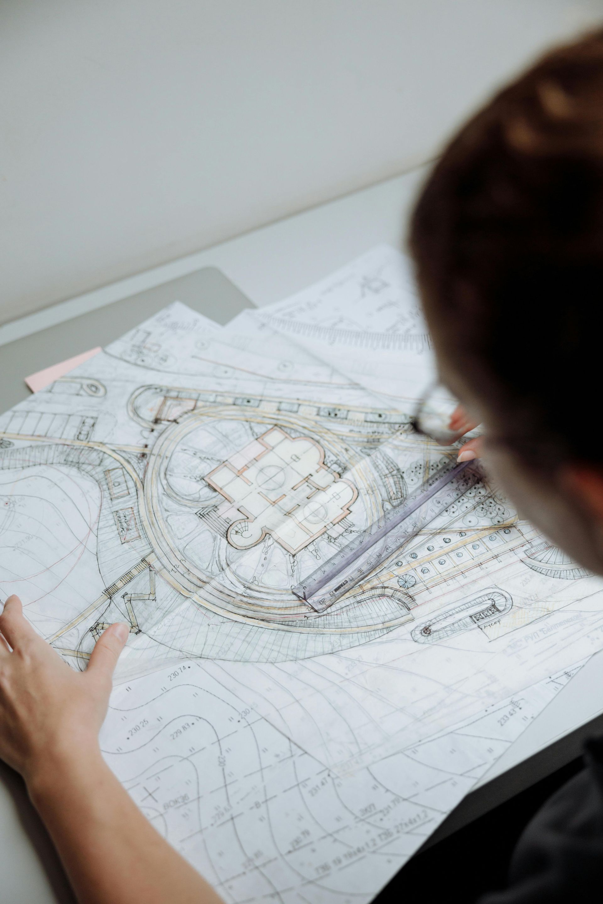 Une personne examine des plans architecturaux sur un bureau, munie d'une règle et d'un crayon.