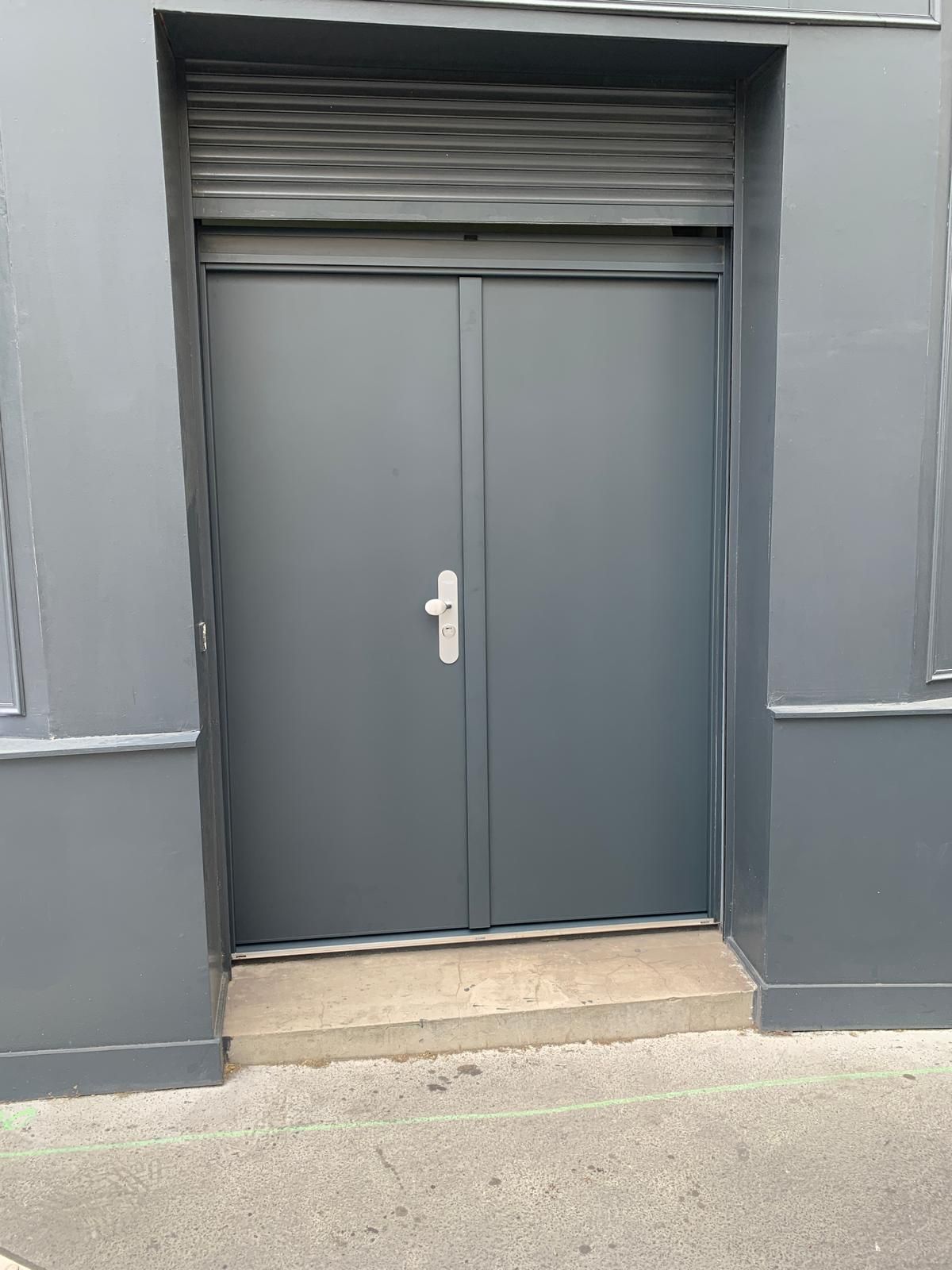 Gros plan sur une porte blindée bleu métal avec serrue grise, murs de la même couleur que la porte