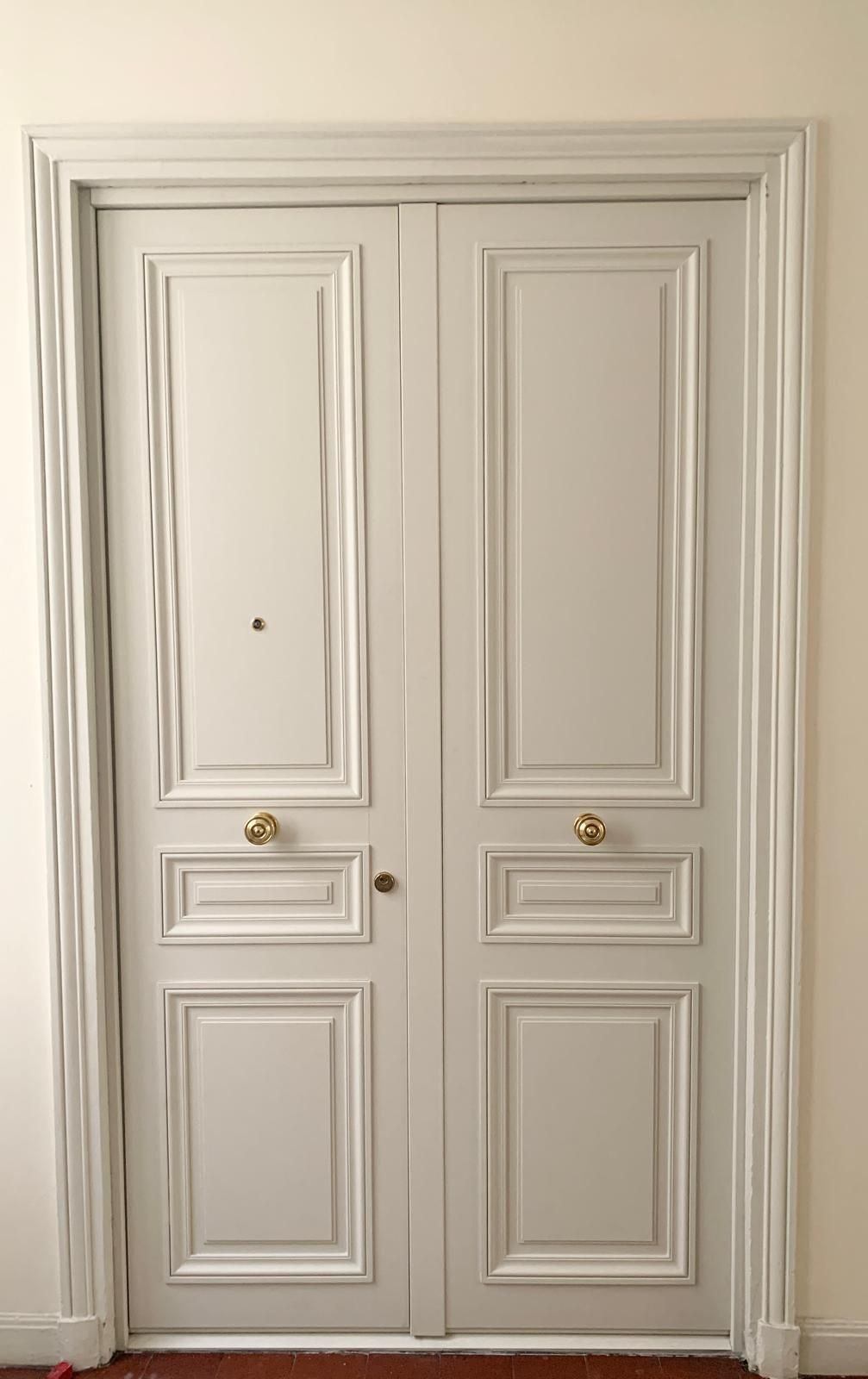 Double porte d'entrée blanche avec poignées dorées dans un couloir beige.