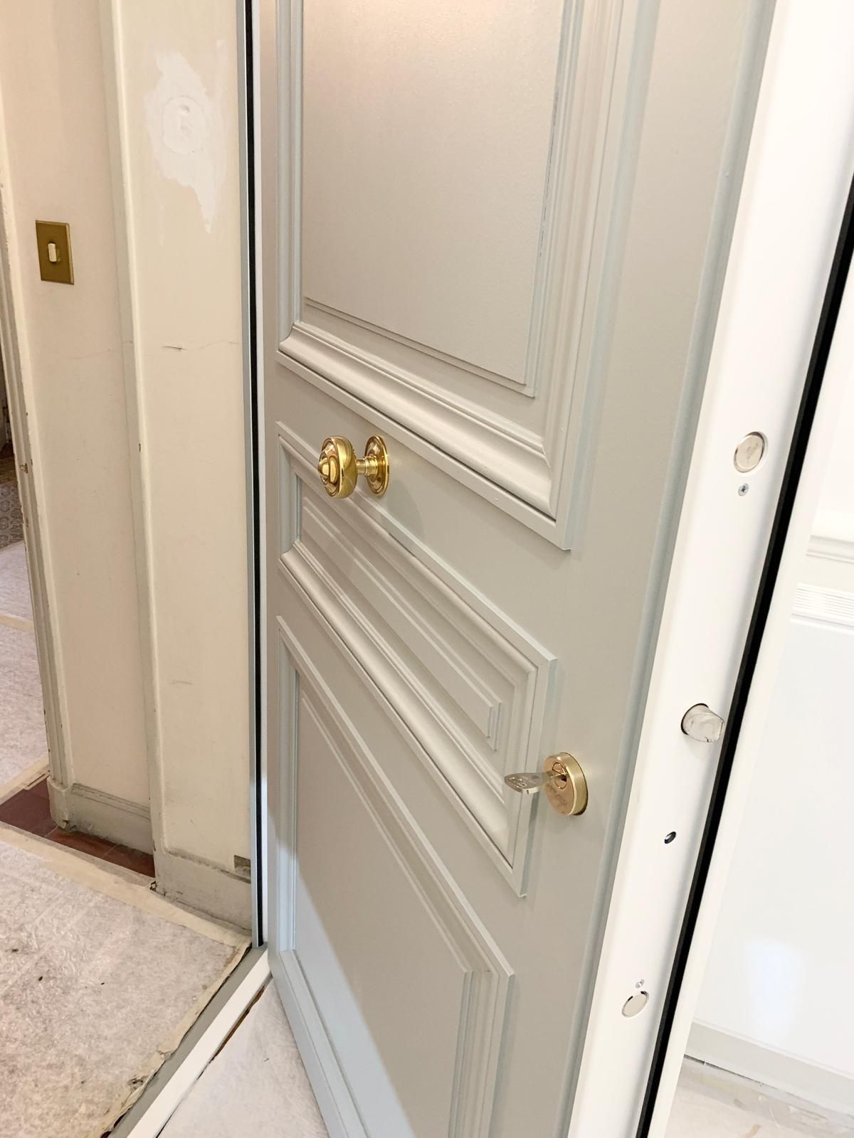 Porte à panneaux blancs partiellement ouverte avec poignées dorées dans un couloir.