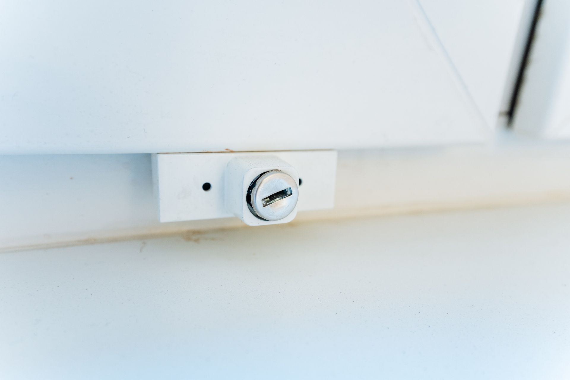 Gros plan sur une serrure en métal blanc sur une fenêtre blanche.