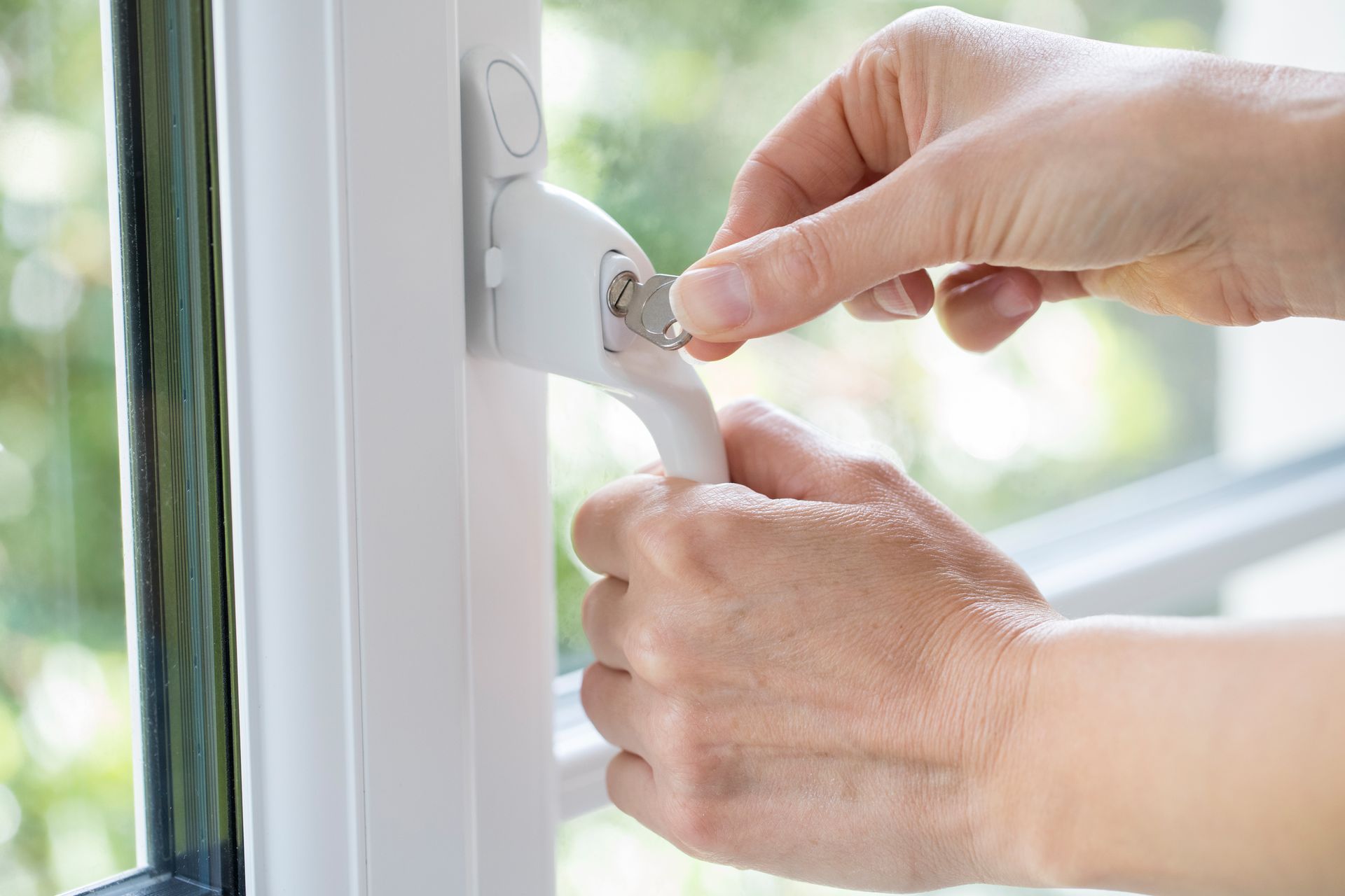 Des mains verrouillent un loquet de fenêtre blanc près d'une fenêtre lumineuse.