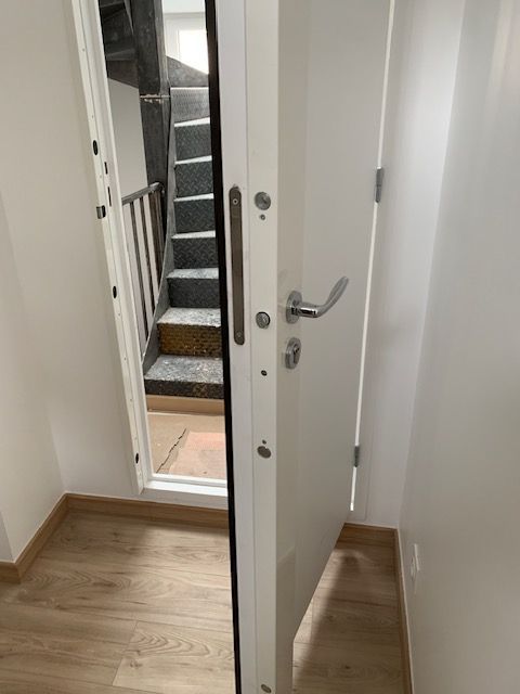 Porte d'appartement blanche ouverte sur un palier avec escalier métallique