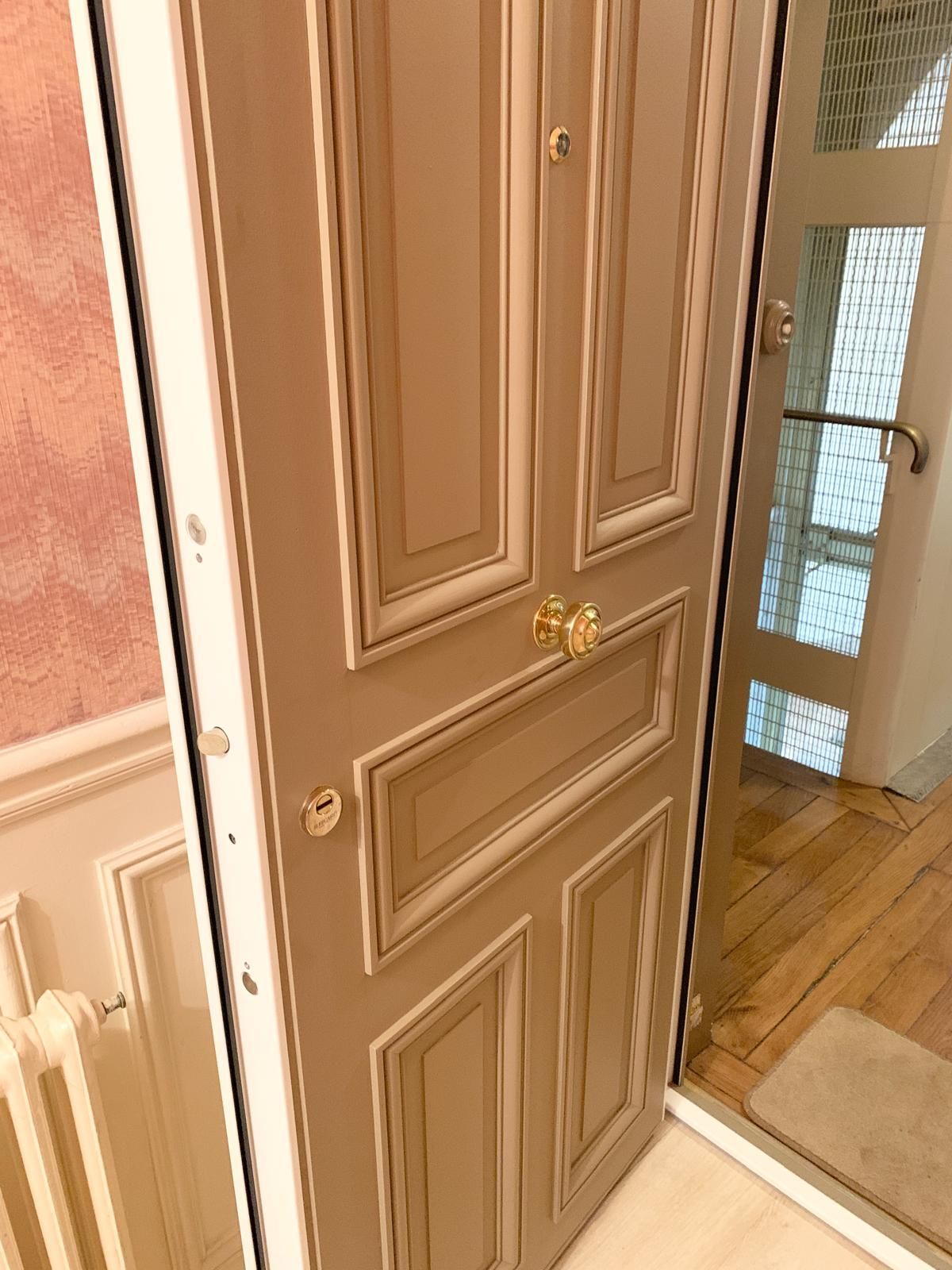 Salon moderne avec canapé beige, étagères en bois, table basse et porte en bois foncé donnant sur la pièce.