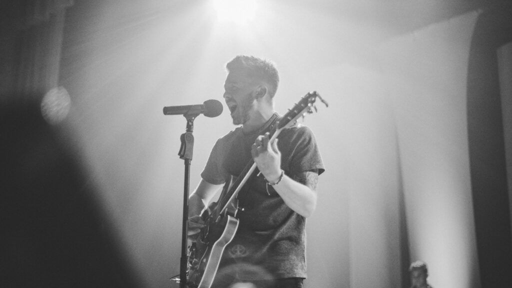Un hombre toca una guitarra y canta con un micrófono en un escenario.