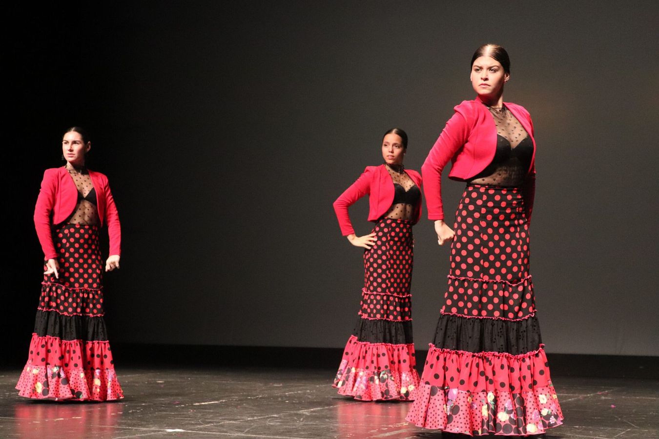 Tres mujeres con faldas de lunares rojos y negros bailan en un escenario.