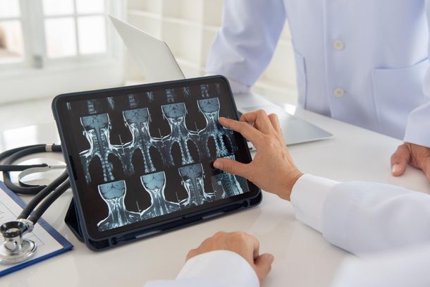 Arzt zeigt in einer hellen Klinikumgebung auf Röntgenbilder auf einem Tablet.