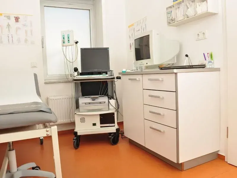 Leeres Untersuchungszimmer mit Bett, Computerwagen, Schränken und orangefarbenem Boden