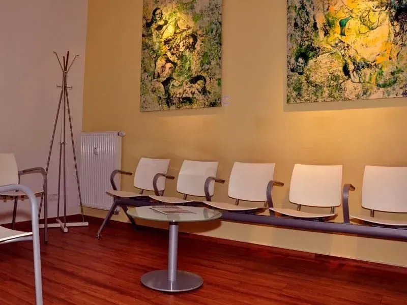 Wartebereich mit weißen Stühlen, rundem Tisch, abstrakter Wandkunst und warmer Beleuchtung auf Holzboden