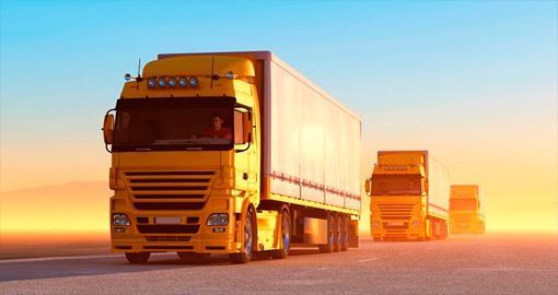 Una fila de camiones semirremolque amarillos circulan por una autopista al atardecer.