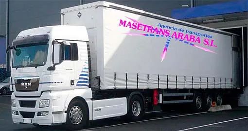 Un camión blanco está estacionado frente a un edificio que dice masettrans araba sl