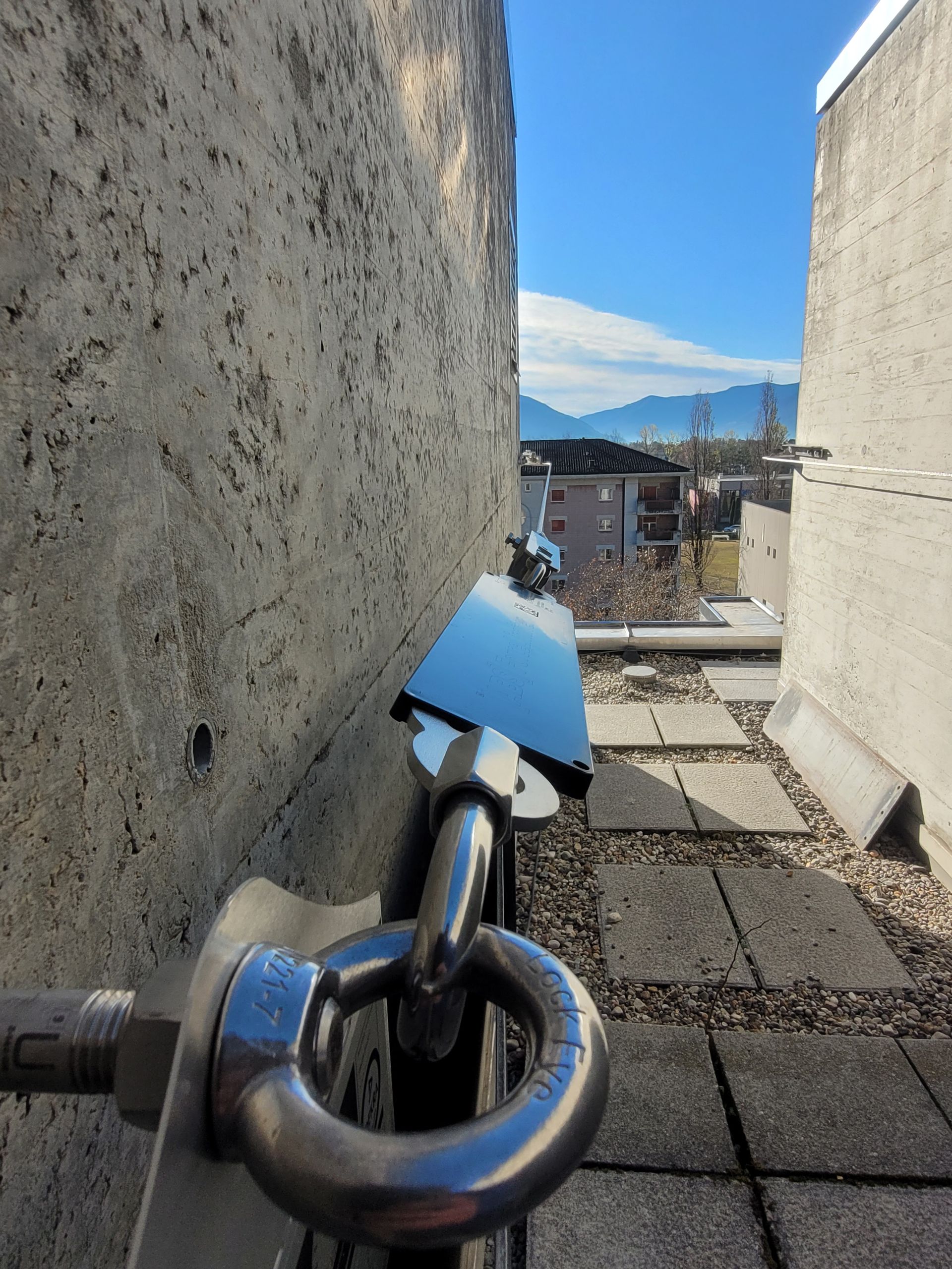 Metallregal; vertikale Träger mit horizontalen, gemusterten Regalböden, grau vor einer hellgrauen Wand.