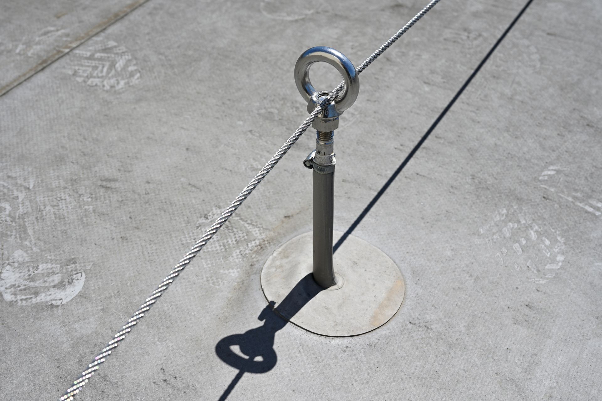 Ein Arbeiter in blauem Sicherheitsanzug, gesichert durch einen Gurt, steht auf einem Dach in der Nähe eines Geländers; im Hintergrund ist die Stadtkulisse zu sehen.