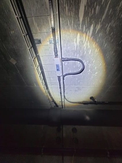 Ein schmaler Durchgang zwischen Betonwänden eröffnet den Blick auf ein Gebäude und Berge unter blauem Himmel.