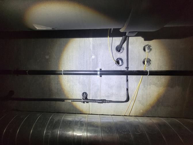 Rohre und Kabel in einem dunklen Industrieraum, beleuchtet von einem Scheinwerfer.