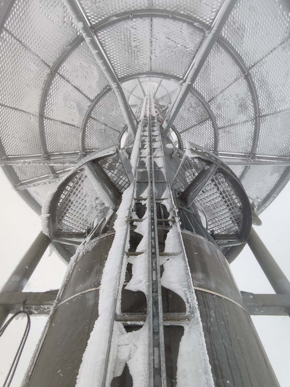 Eine Person befindet sich auf einer Metallplattform und trägt einen an einer Stange befestigten Sicherheitsgurt.