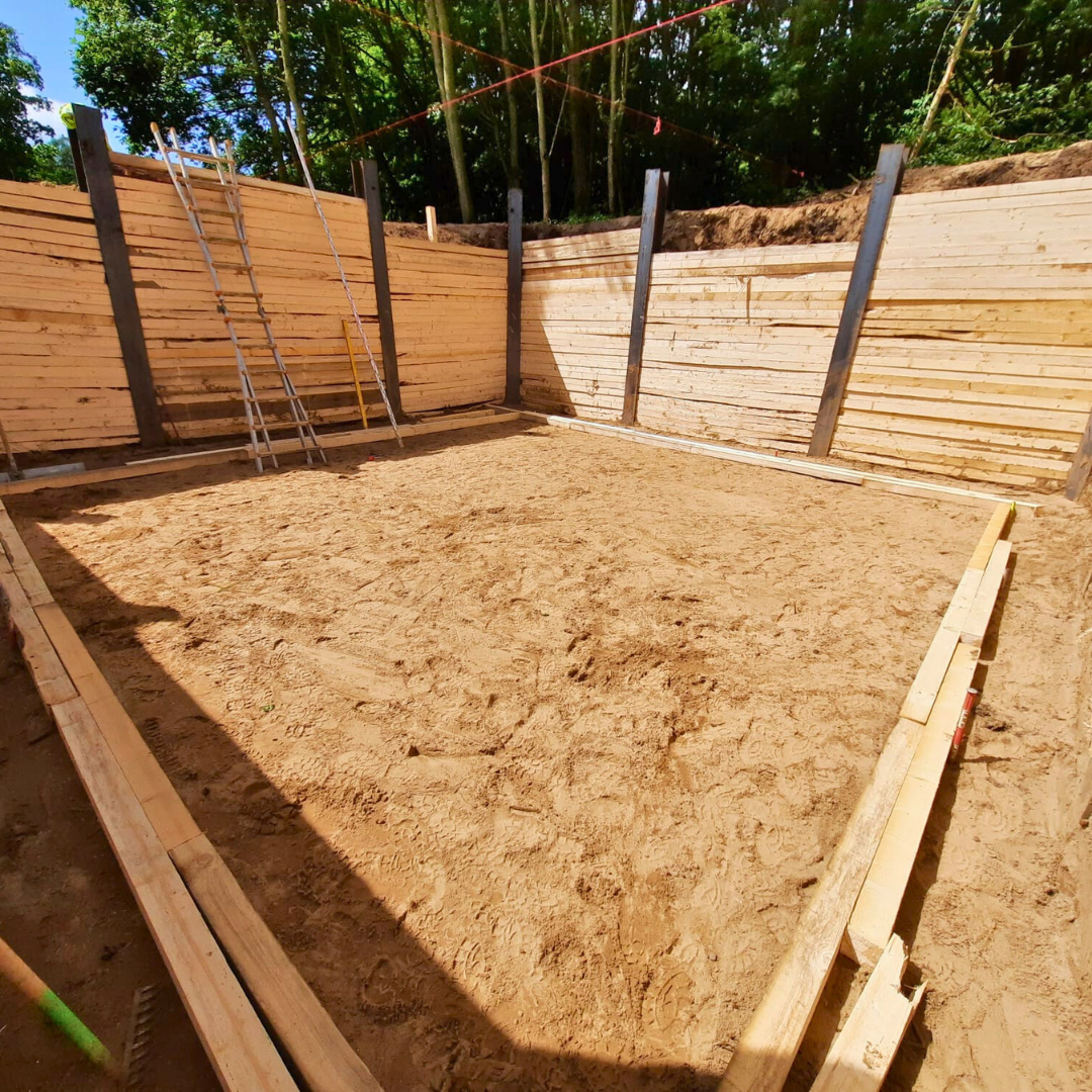 Ein Holzzaun umgibt eine Sandfläche mit Bäumen im Hintergrund