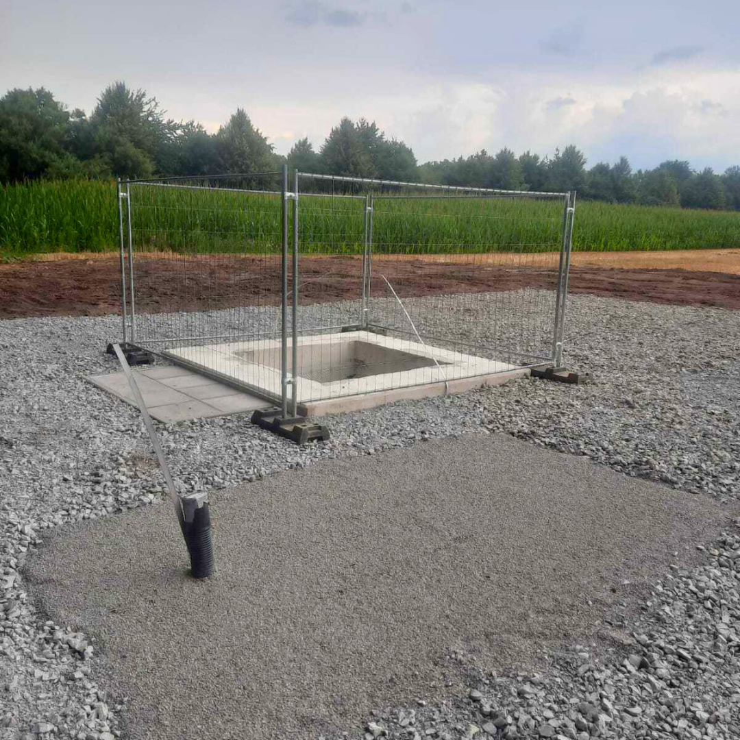 Ein Loch im Boden mit einem Zaun darum und einem Feld im Hintergrund