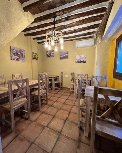 Acogedor comedor rústico con mesas y sillas de madera, suelo de baldosas de terracota y vigas de techo a la vista.