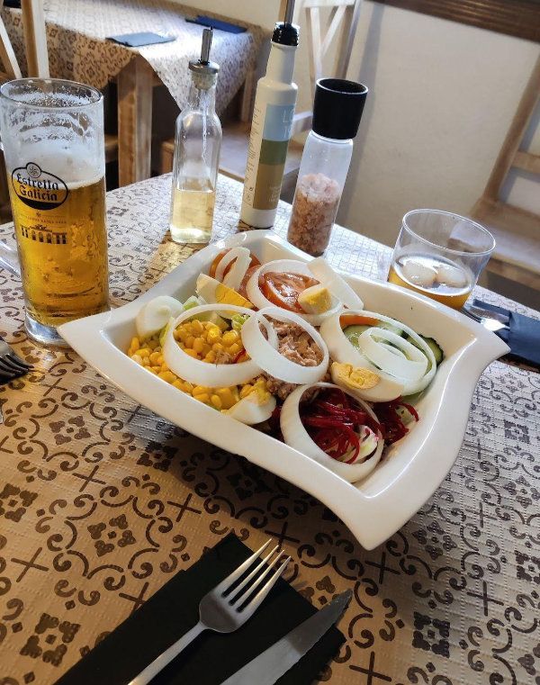 Plato de ensalada con huevos en rodajas y verduras sobre la mesa de un restaurante, junto a un vaso de cerveza.