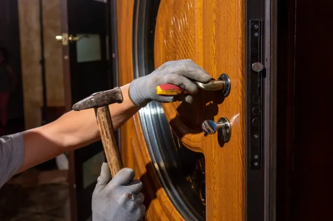Un trabajador con guantes utiliza un martillo para instalar o ajustar la manija de una puerta de madera.
