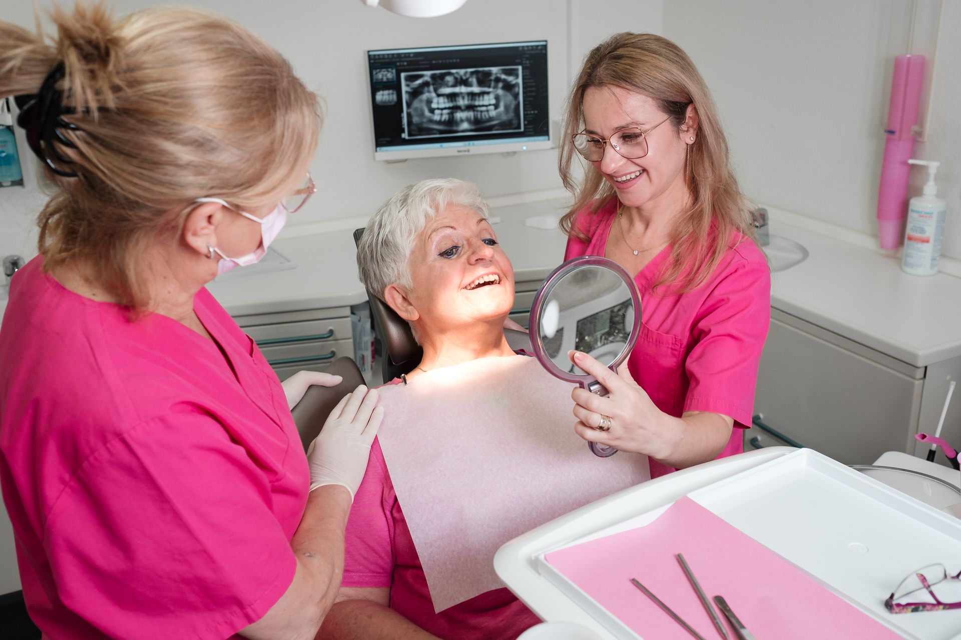 Eine Zahnärztin zeigt einer Patientin ihre Zähne im Spiegel. Die Frau lächelt in einer Zahnarztpraxis.