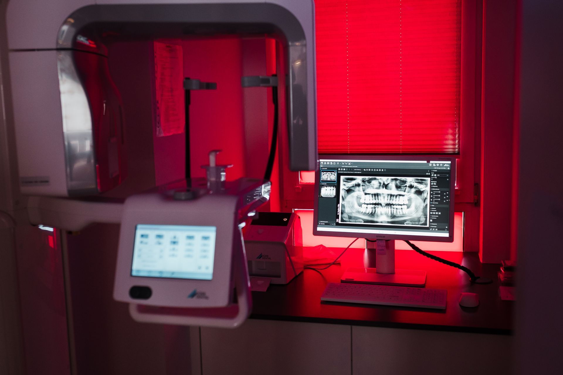 Ein zahnärztliches Panoramaröntgengerät mit einer digitalen Anzeige, auf der ein Zahnscan angezeigt wird. Die Umgebung ist in rotes Licht getaucht.