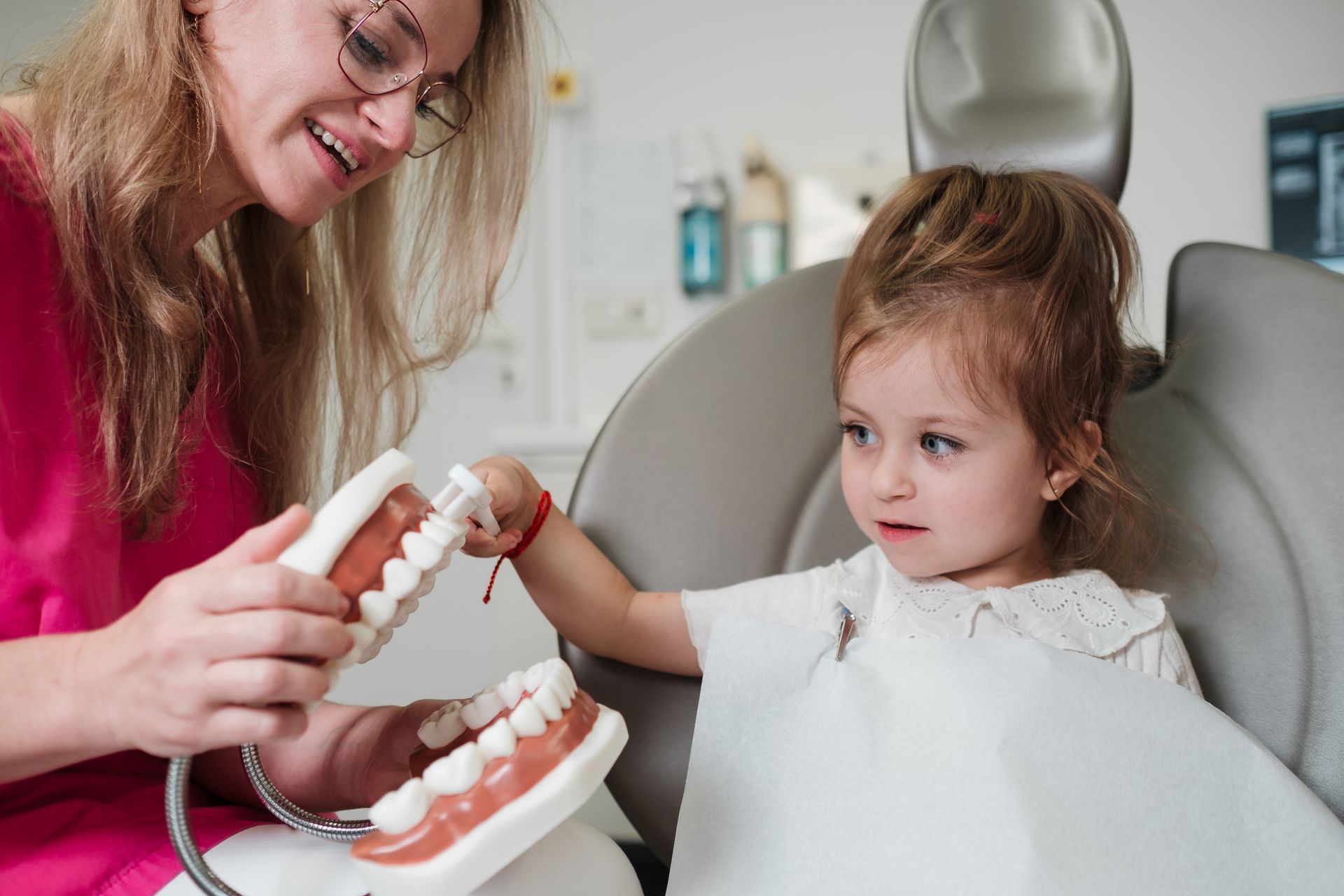 Zahnarzt zeigt einem jungen Mädchen ein Zahnmodell. Das Mädchen sitzt auf einem Zahnarztstuhl und betrachtet das Modell.