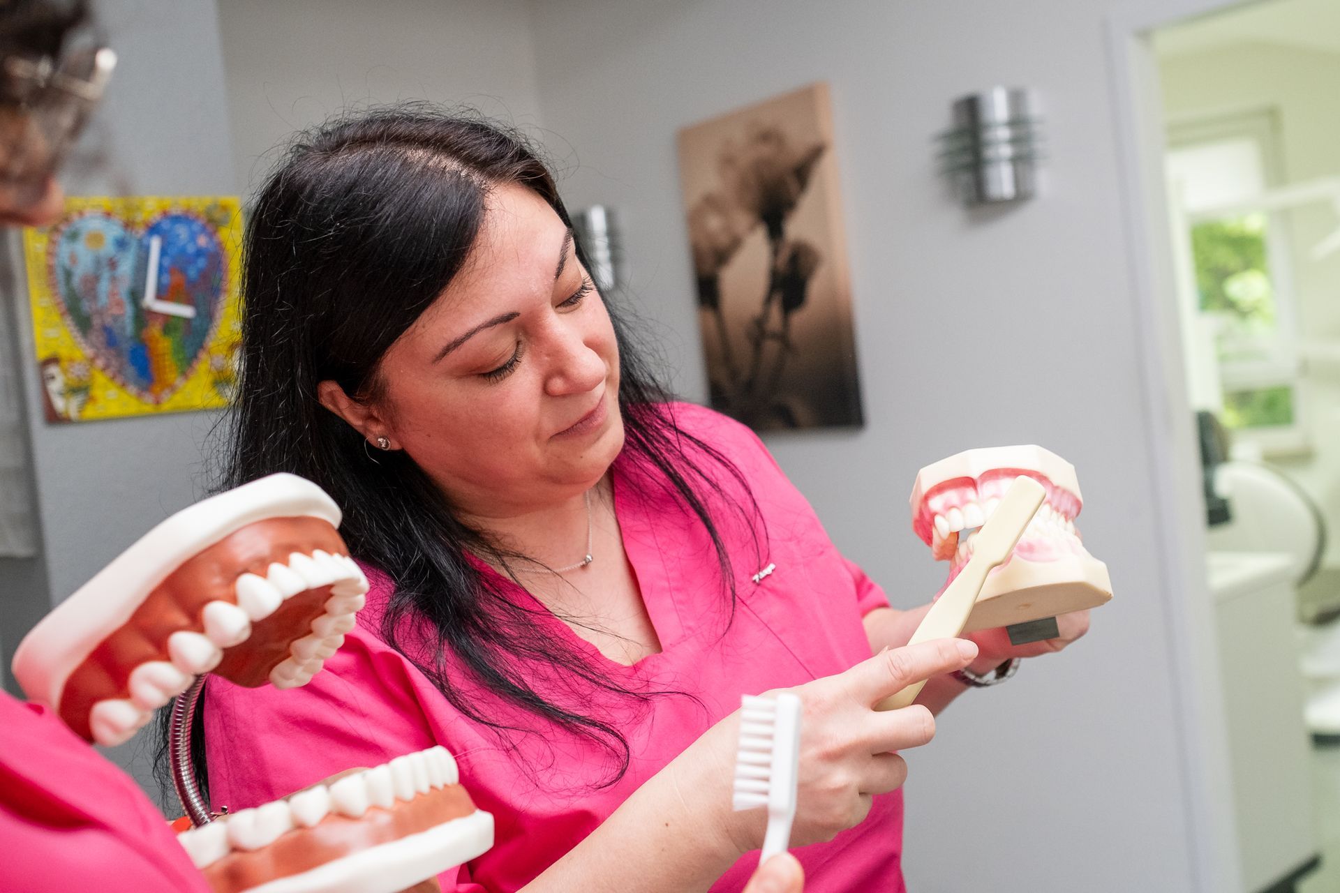 Ein Zahnarzt in einer rosa Uniform demonstriert in einer Zahnarztpraxis das Zähneputzen an einem Zahnmodell.