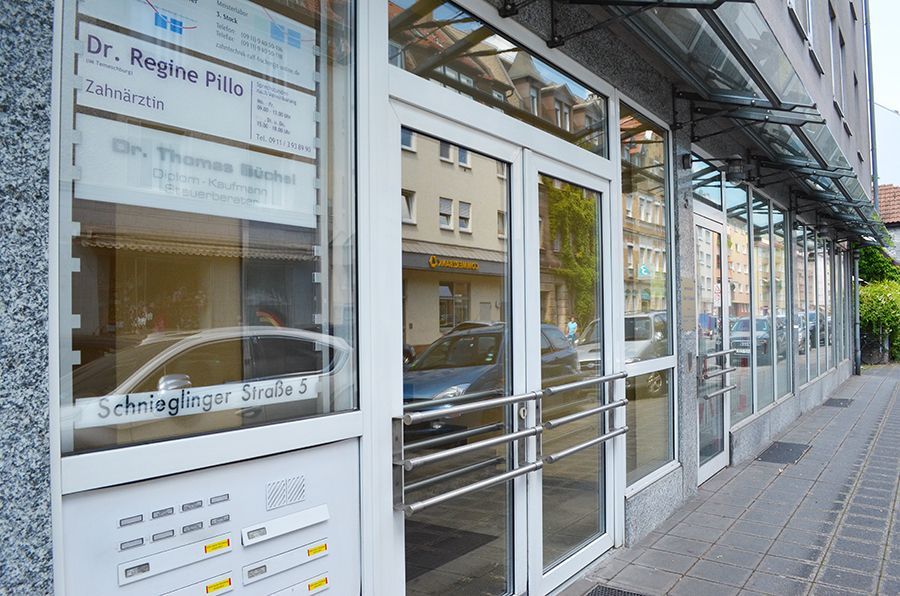 Außenansicht eines Arztpraxisgebäudes mit Glastüren, Beschilderung für Dr. Pillo und Dr. Henschel und der Straßenadresse „Schnieglinger Straße 2“.