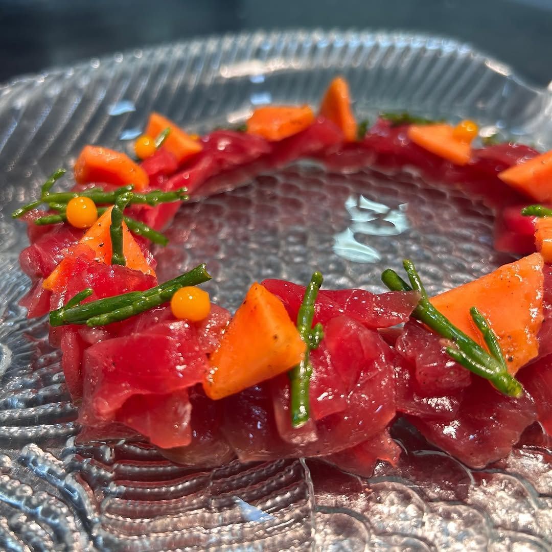 Tartar de atún rojo dispuesto en forma de anillo sobre un plato de cristal, adornado con zanahoria y cebollino