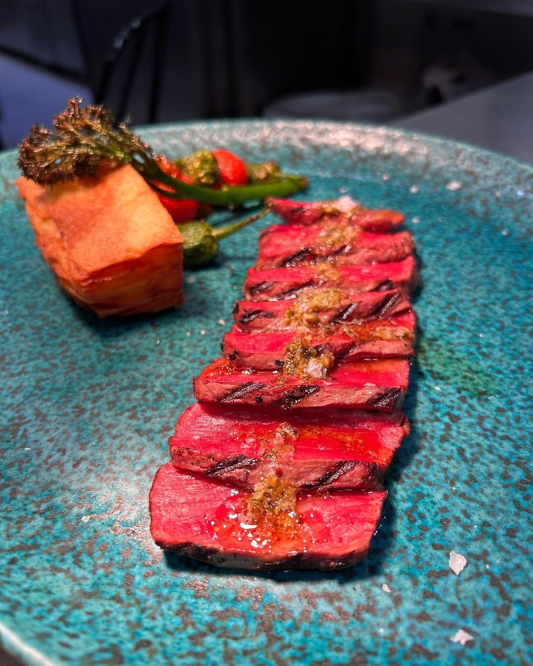 Filete sellado en rodajas sobre un plato turquesa con verduras y guarnición con salsa.