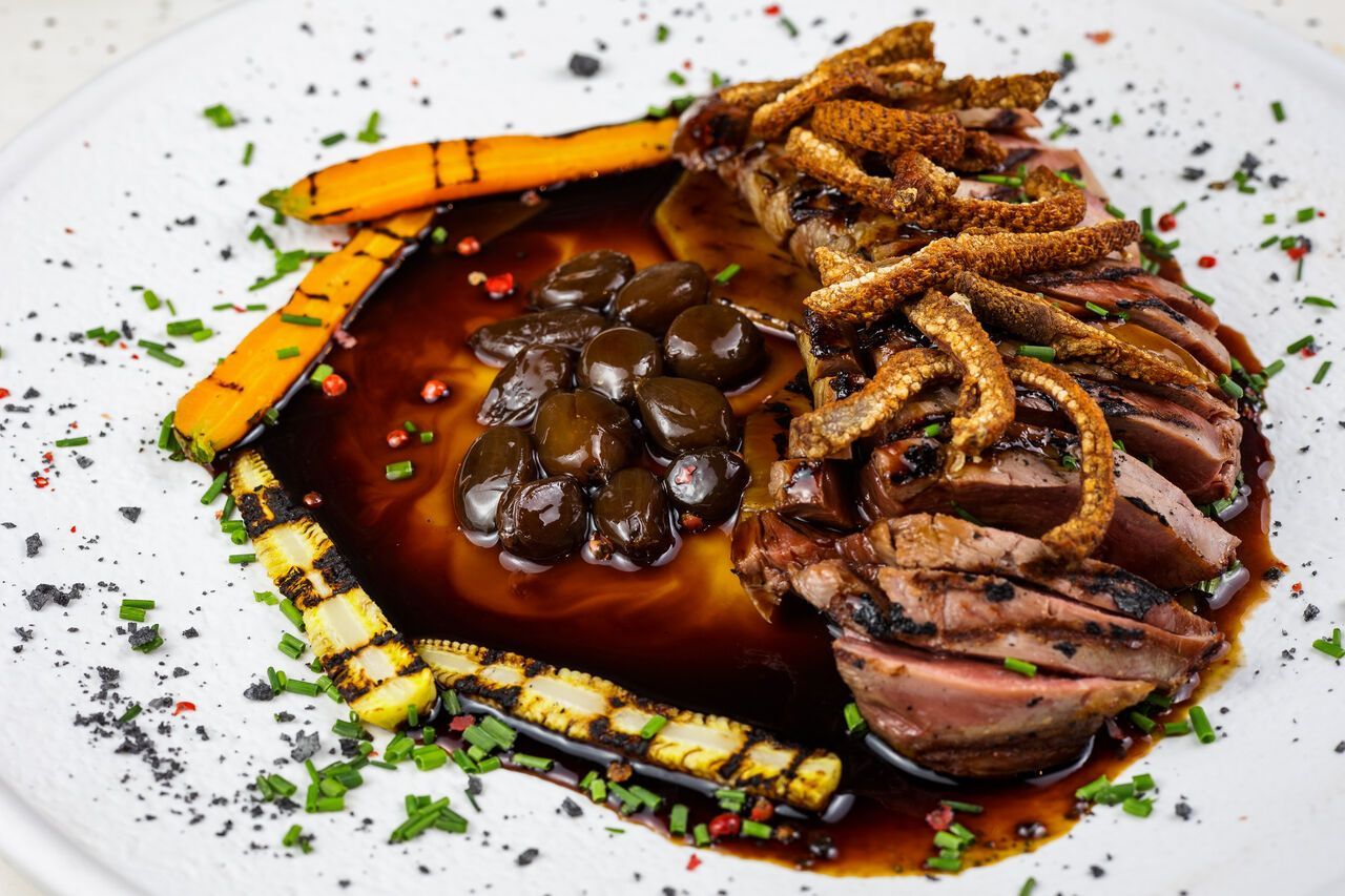 Filete emplatado con salsa, champiñones y verduras asadas en un plato blanco.